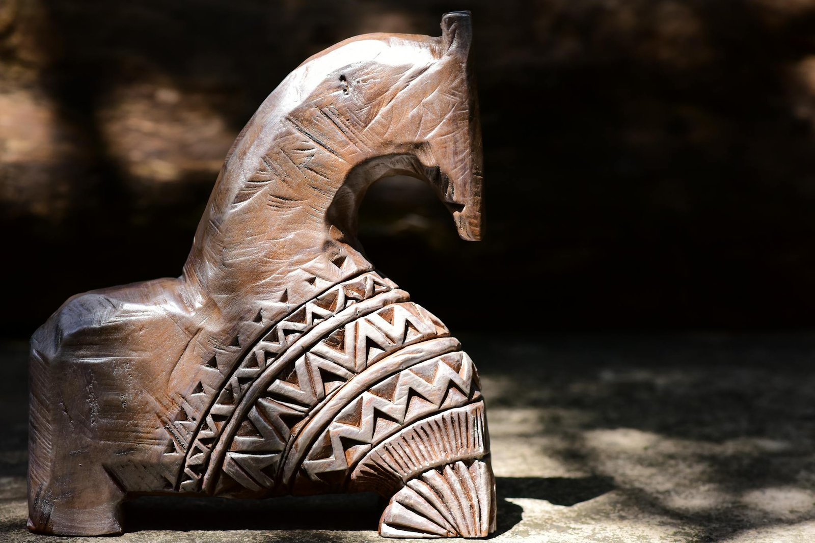 Close-up of a hand-carved wooden horse sculpture with tribal patterns, capturing natural light and shadows.